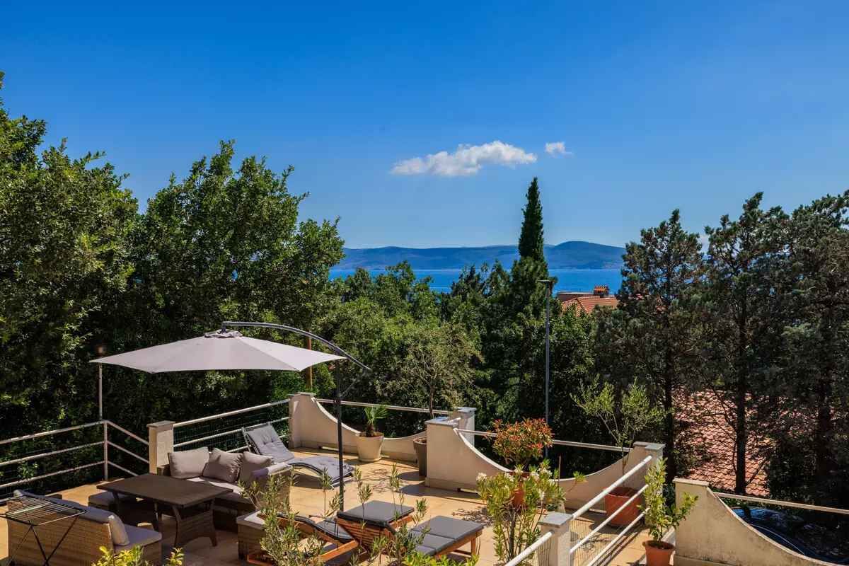 A rooftop terrace with outdoor furniture, a large umbrella, and a view of the sea.