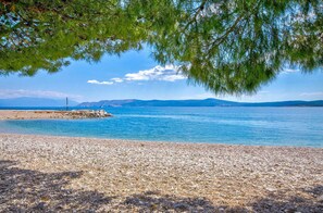 A pebble beach with clear blue water and distant mountains. - Holiday apartment with terrace and sea view (Crikvenica)