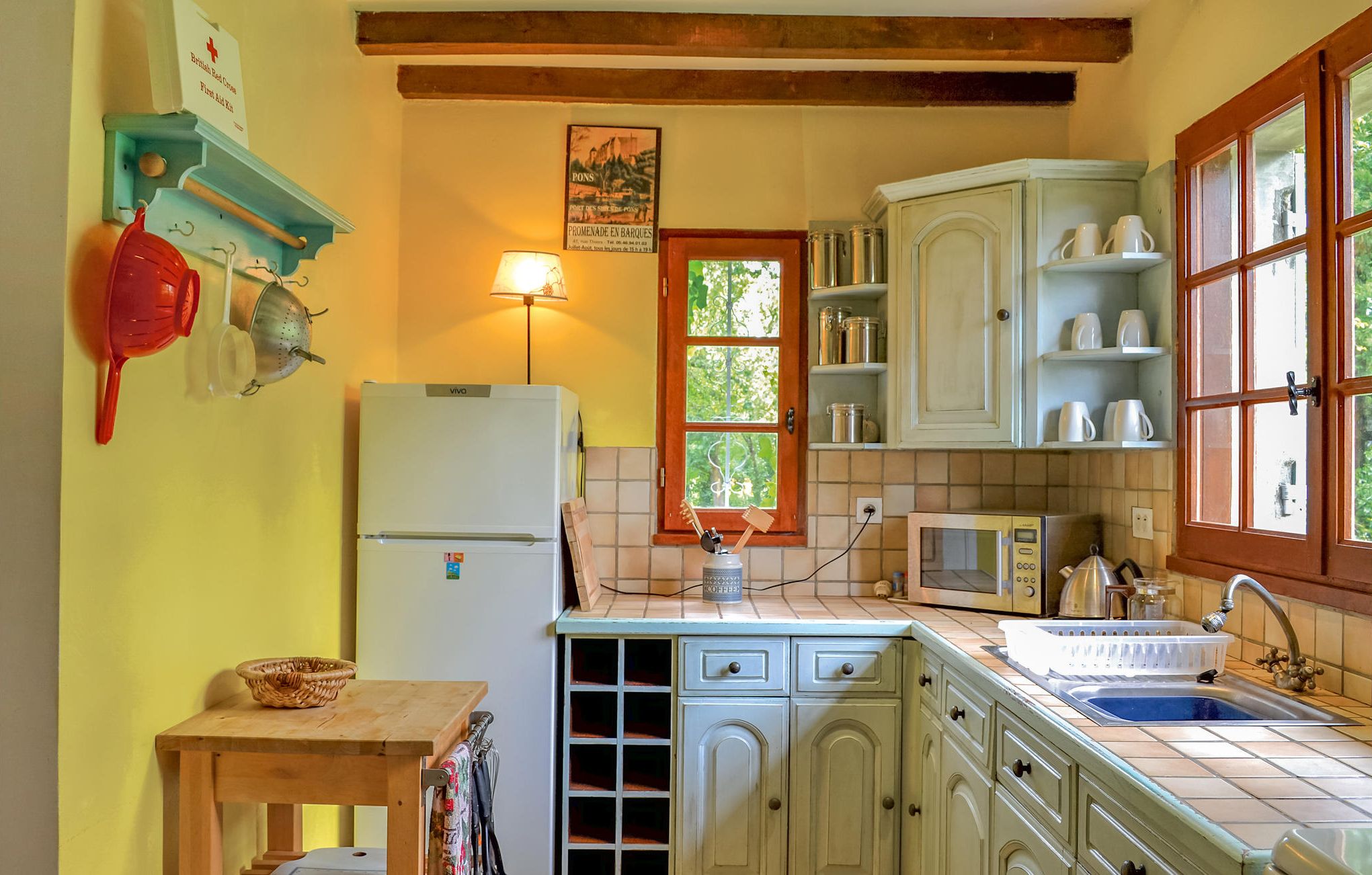 A kitchen with a white refrigerator, wooden cabinets, a sink, and a window with a view of trees.