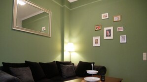 Un salon avec un canapé de couleur sombre, une table basse en bois, un lampadaire et plusieurs tableaux encadrés accrochés au mur.