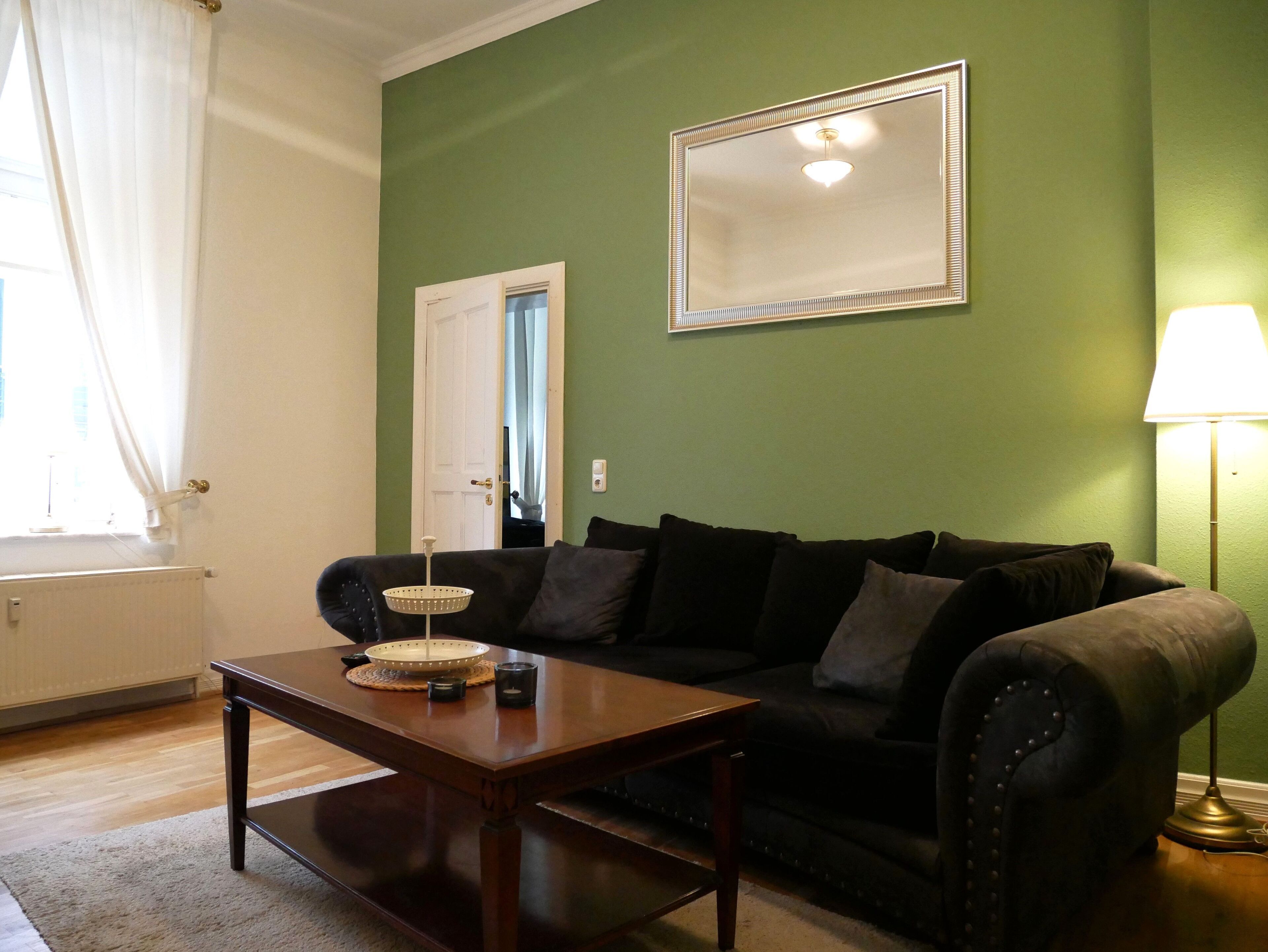 Un salón con un sofá marrón oscuro, una mesa de centro de madera y una pared verde.