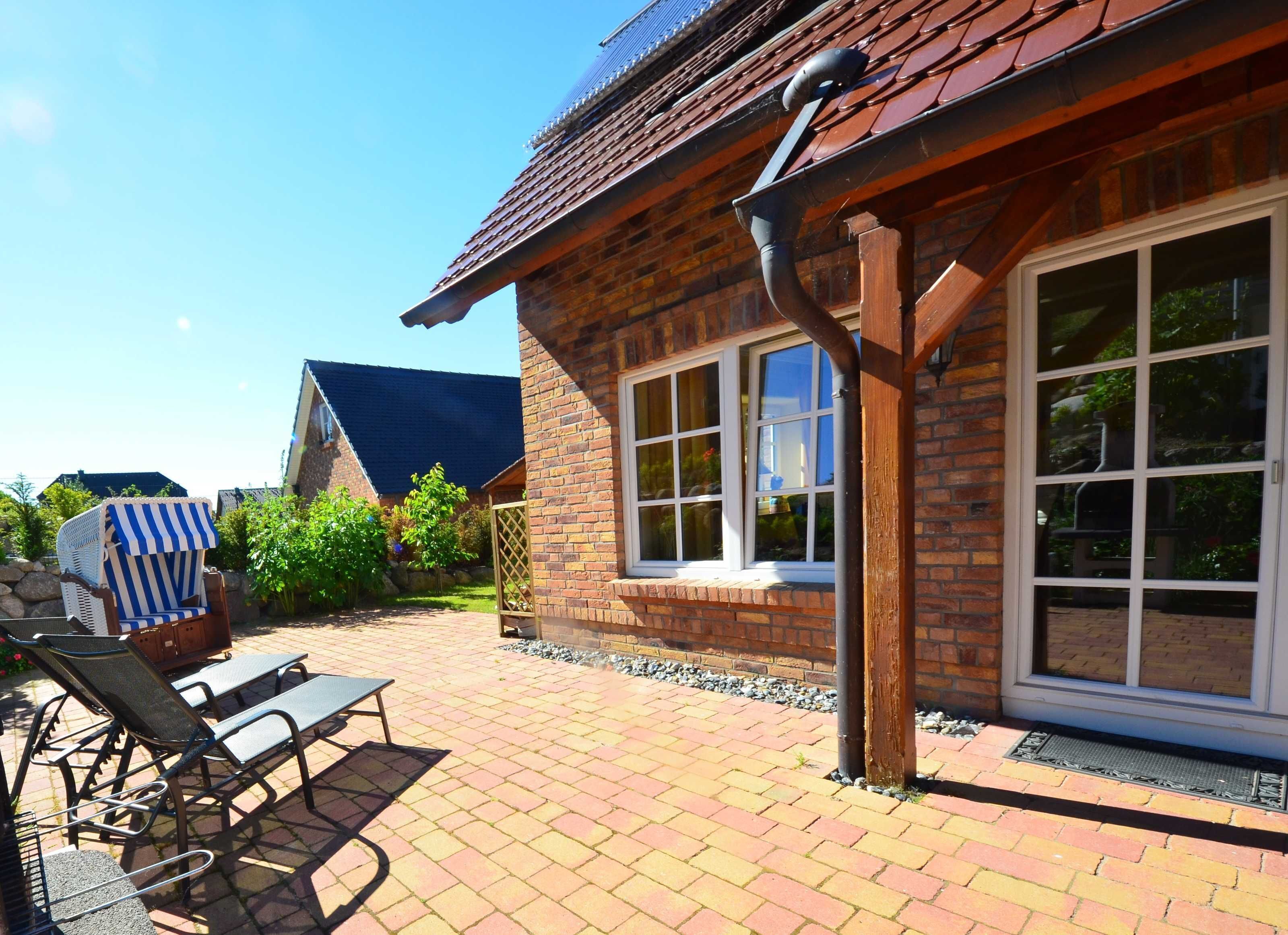 A brick house with a large window, a covered patio with lounge chairs, and a blue awning in the background.