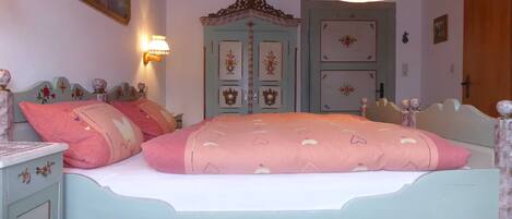Quarto com cama, mesa de cabeceira, penteadeira, espelho e porta com painéis decorativos.