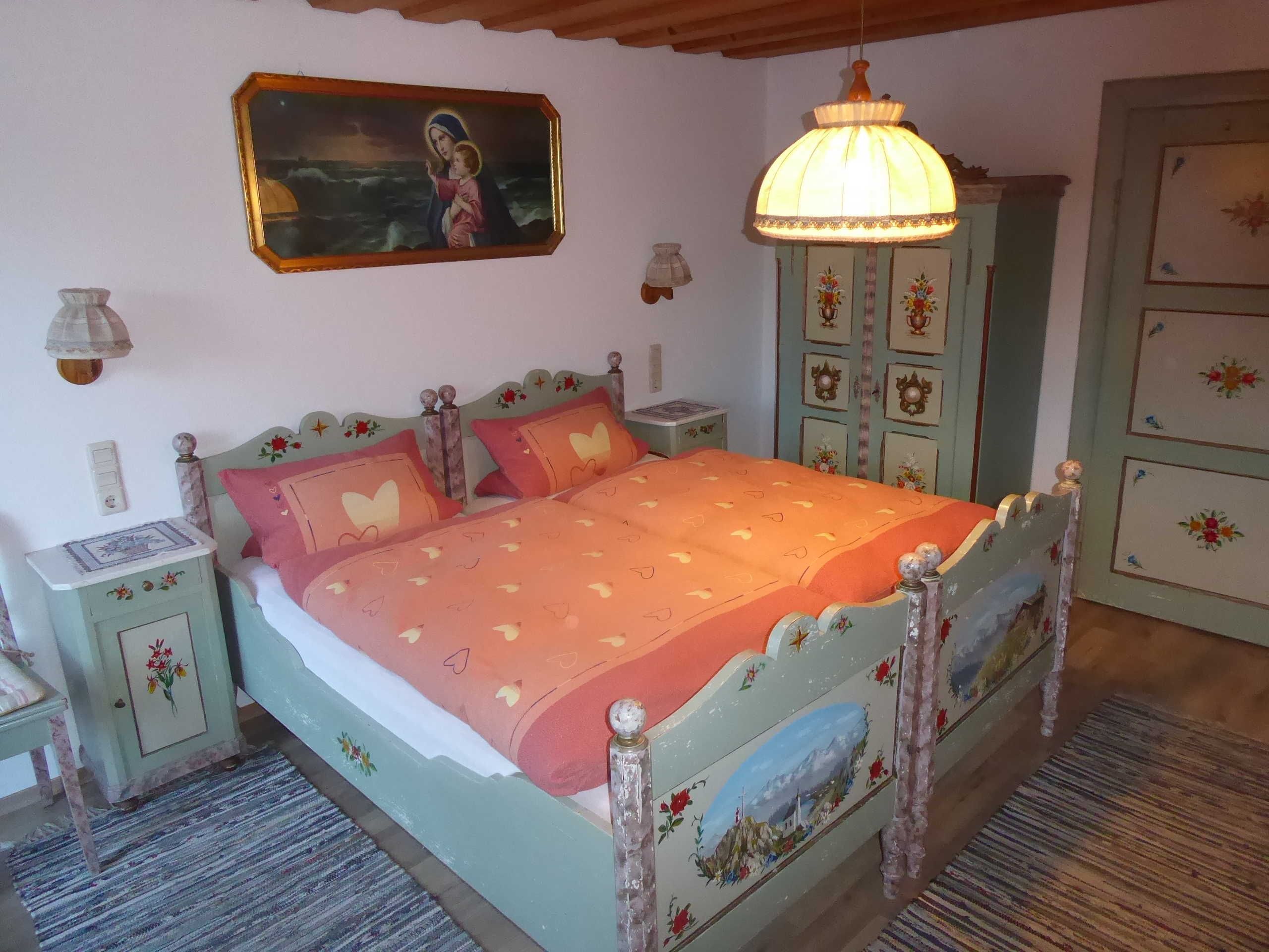Ein Schlafzimmer mit Bett, Nachttischen, einem Schminktisch und einem Hängeleuchter, sowie einem Gemälde.