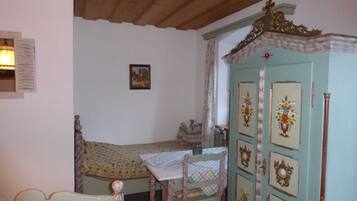 Ein Zimmer mit einem Bett, einem Tisch mit kariertem Tischtuch, einem Schrank mit Verziertungen und einer Holzboden.