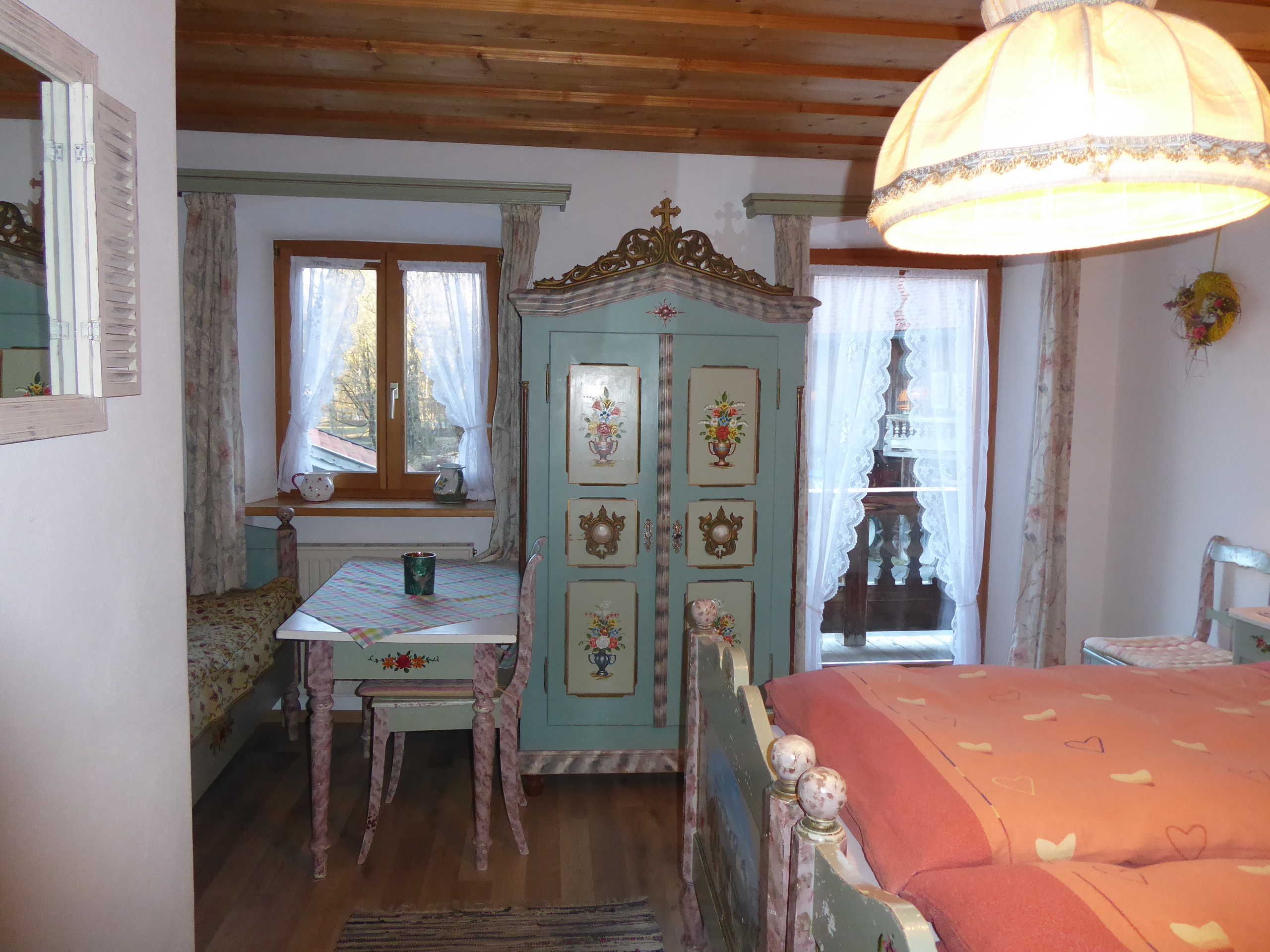 Ein Zimmer mit einem Bett, einem Tisch, einem Stuhl, einem Kleiderschrank und einem fenster mit Vorhängen.
