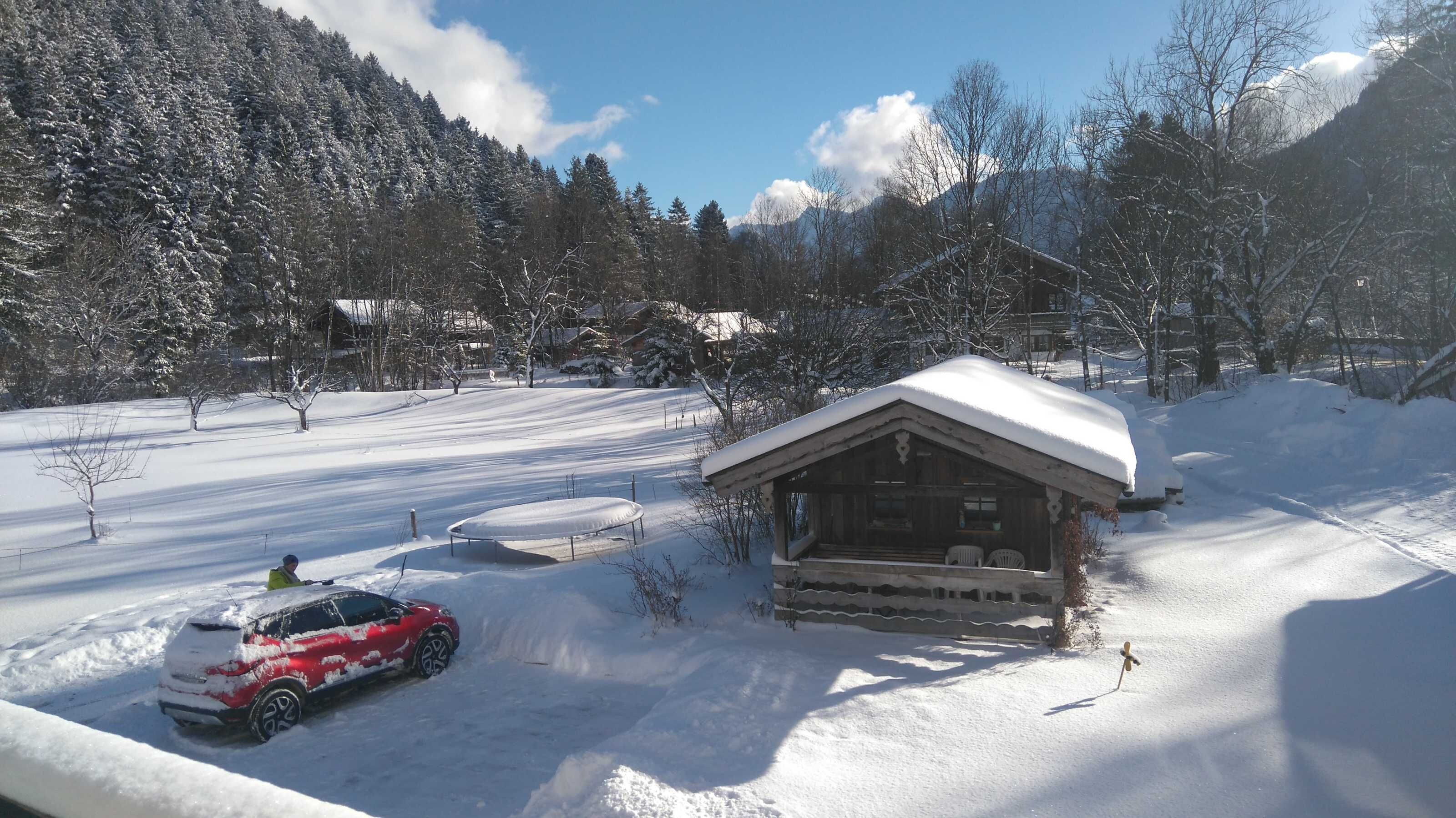 Eine Hütte mit schneebedecktem Dach, umgeben von verschneiter Landschaft und Bäumen.