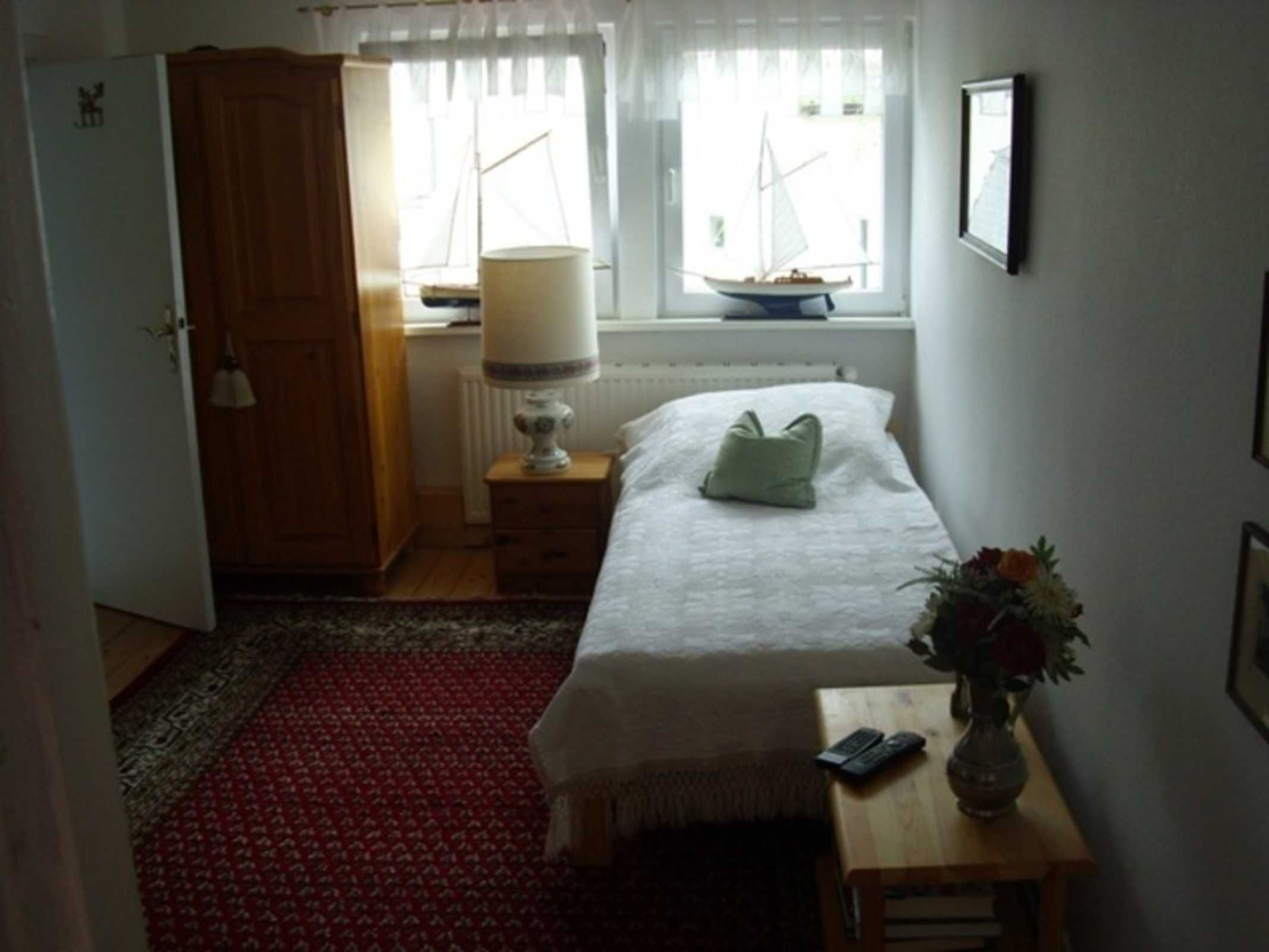 Quarto com cama, mesa de cabeceira, abajur e janela com vista para um veleiro.