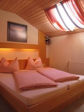 Una cama doble con ropa de cama rosa, un cabecero de madera, un cuadro en la pared y una ventana con cortinas.