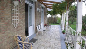 A covered porch with a bench and a wicker chair, a brick wall, and a sign reading "LA PERGOLA". - 2 bedroom amazing home in Houlle (Houlle)
