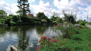 A calm river with a wooden dock, lush greenery, and a house in the background. - 2 bedroom amazing home in Houlle (Houlle)