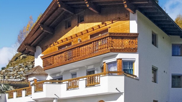 A multi-story building with a white facade, wooden balconies with intricate railings, and a stone wall on the left side. - Ferienwohnung mit top Ausblick (Kappl)