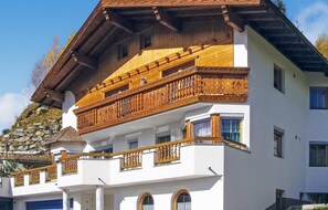 Een meerhoog gebouw met een witte gevel, houten balkons met gedetailleerde hekwerken en een stenen muur aan de linkerzijde.