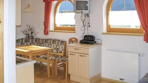 A compact room with a wooden table and bench, two windows with curtains, a television mounted on the wall, and a radiator. - Ferienwohnung mit top Ausblick (Kappl)