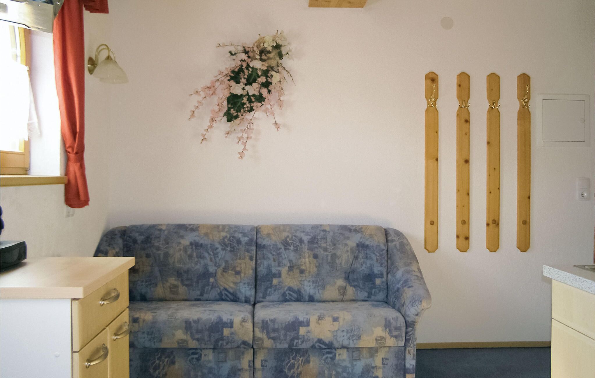 Ett rum med en blå soffa med mönster, ett väggfäst skidhållare och ett litet fönster med en gardin.
