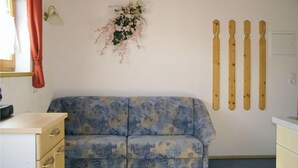A room with a blue patterned sofa, a wall-mounted ski rack, and a small window with a curtain. - Ferienwohnung mit top Ausblick (Kappl)