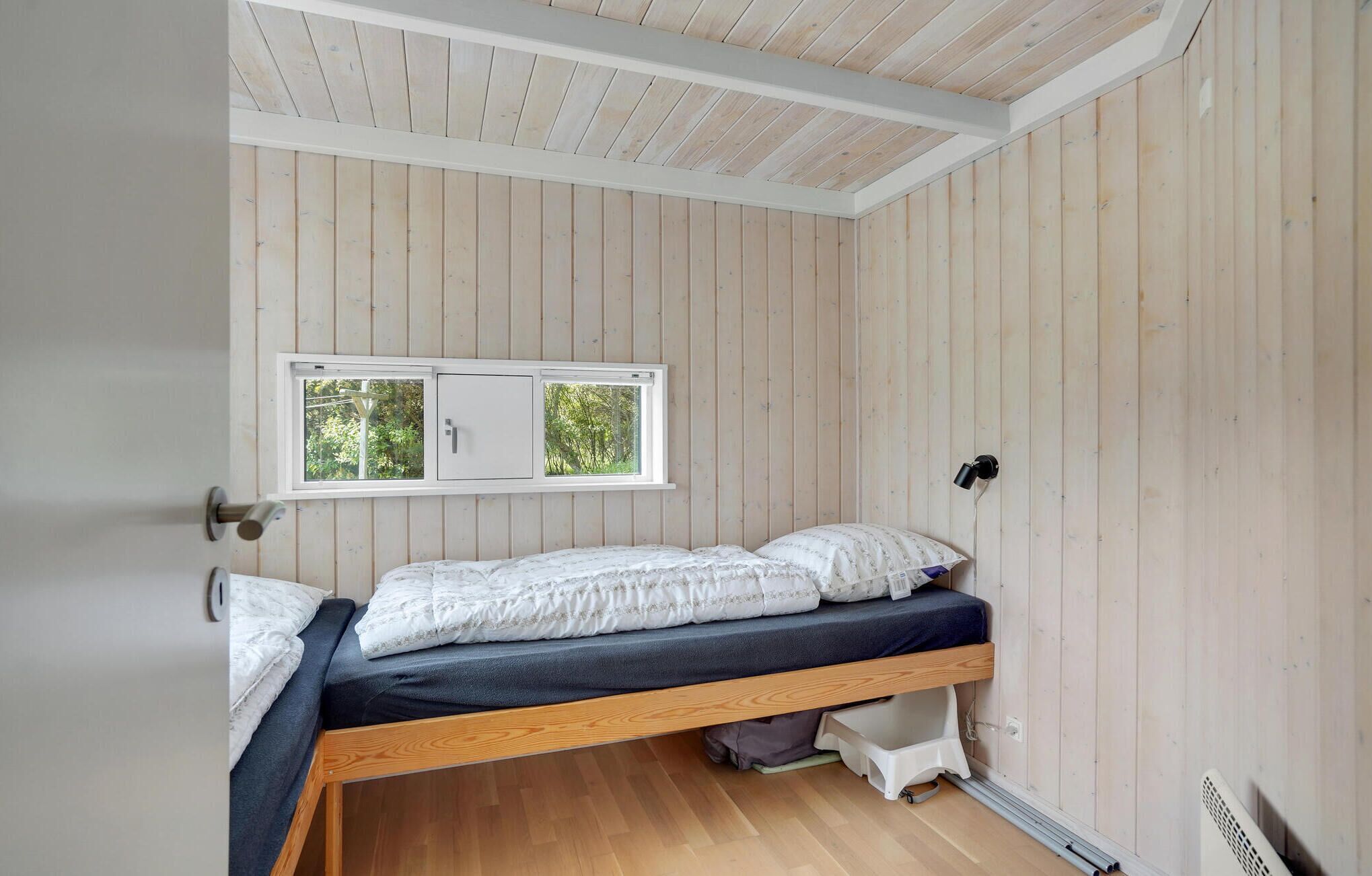 Une petite chambre avec un lit simple et un lit superposé en bois, une fenêtre donnant sur un paysage verdoyant et un plafond blanc.