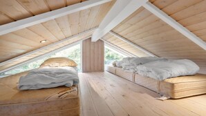 Un pequeño dormitorio en ático con dos camas, pisos de madera y techo inclinado.