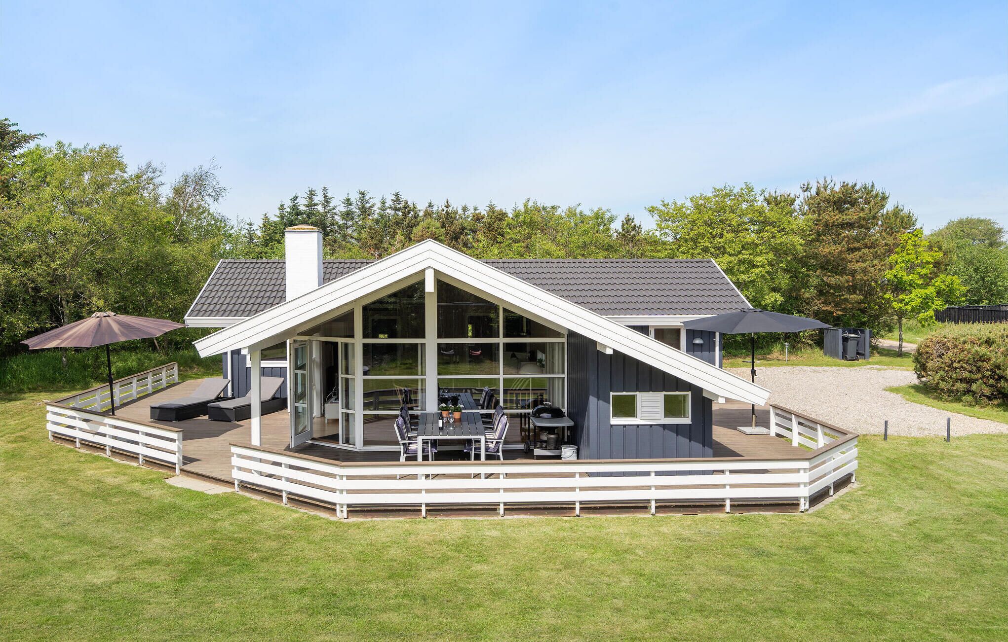 A modern house with a large deck, a covered patio, and a view of the surrounding greenery.