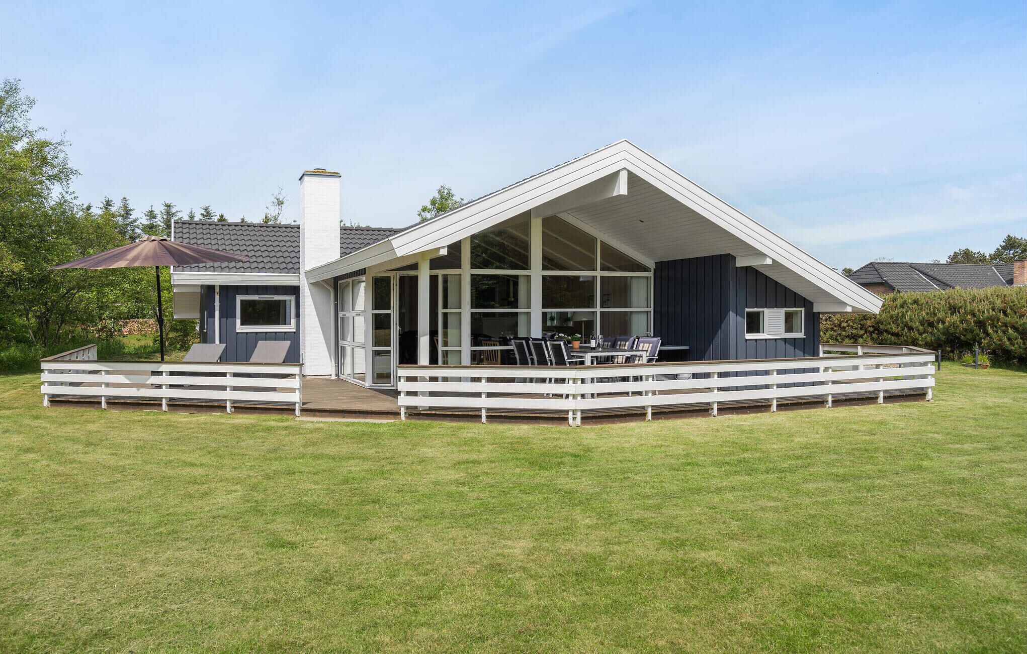 A modern house with a large glass front, a covered patio, and a white fence.