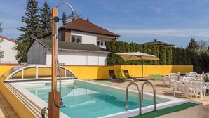Piscina com deck de madeira, espreguiçadeiras e parede amarela.