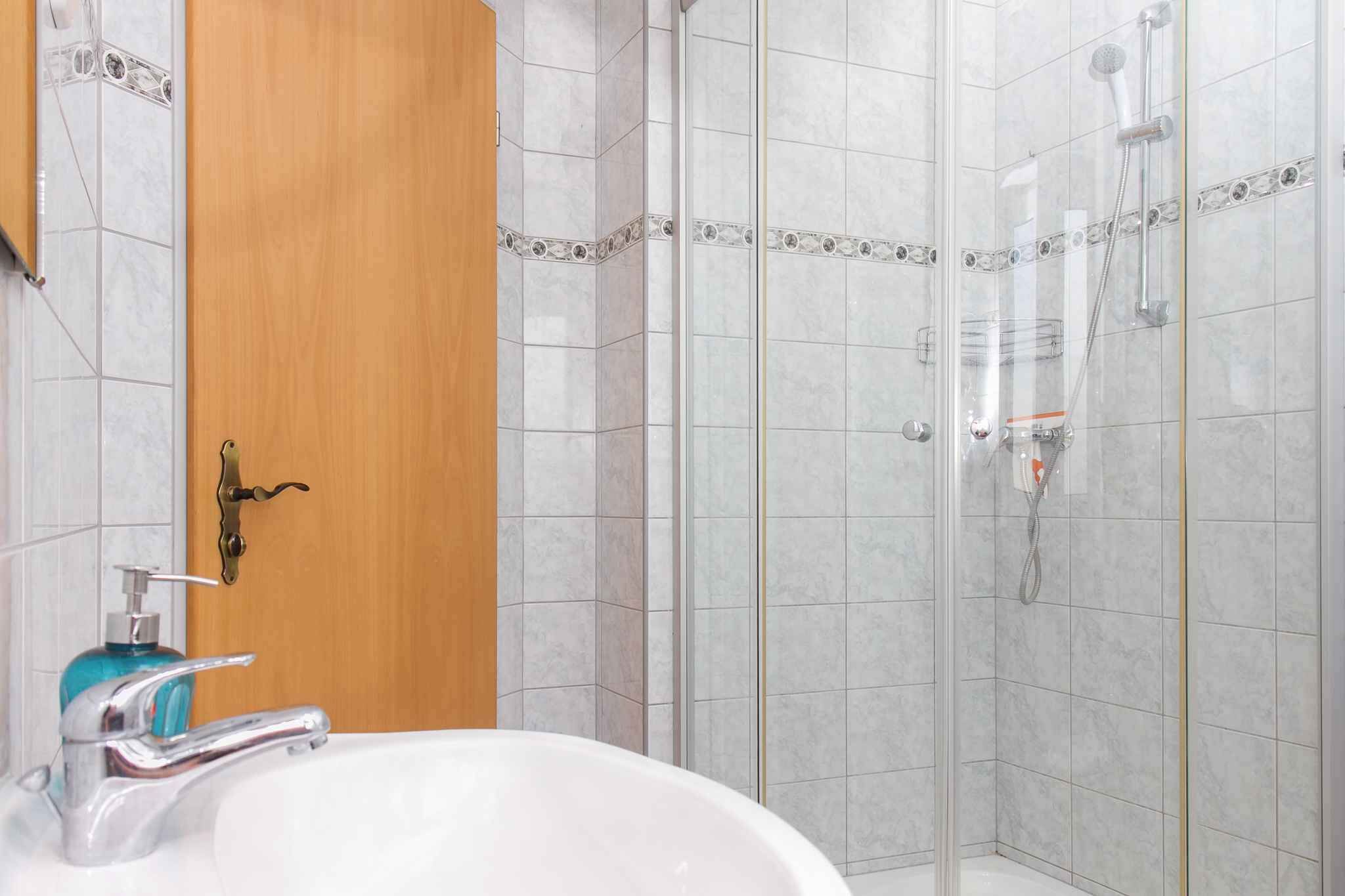 Ein Badezimmer mit einem weißen Waschbecken, einer Holztür und einer Duschkabine.