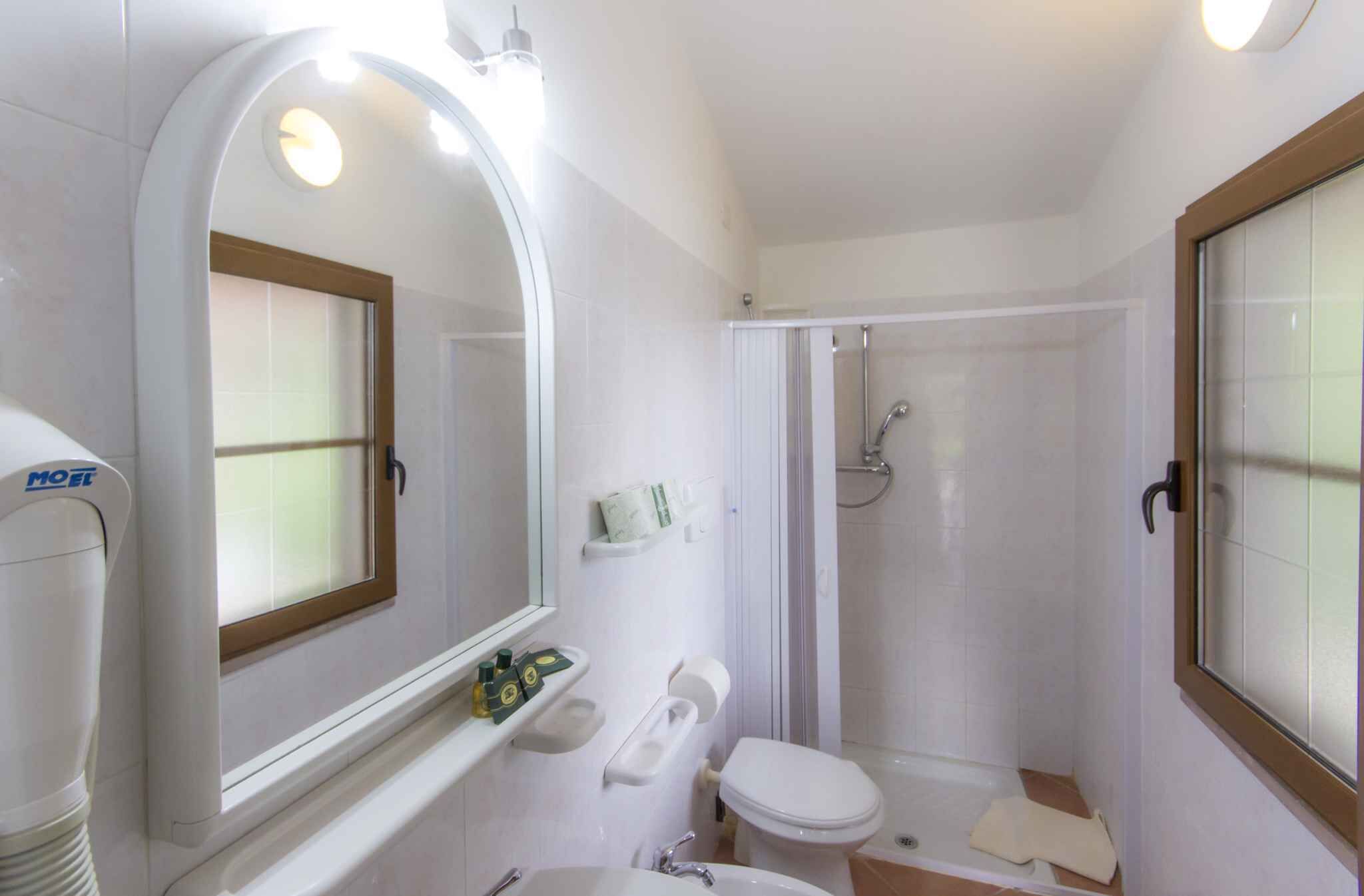 A compact bathroom with a toilet, sink, and shower. There is a mirror with a wooden frame, and a towel rack is visible.