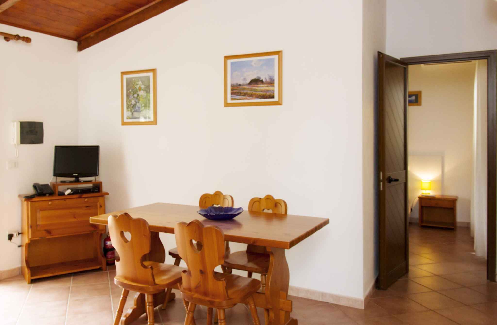 A dining area with a wooden table and chairs, a television on a stand, and two framed pictures on the wall.