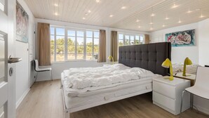Quarto com uma cama grande, uma escrivaninha, uma cadeira, mesa de cabeceira com luminárias e um quadro na parede.
