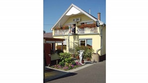 A two-story house with a balcony, a front door, and a small garden with flowers.