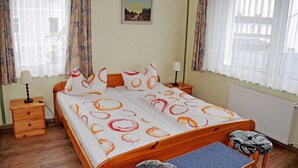 Un dormitorio con una cama de madera, una mesita de noche con lámpara, una pequeña mesa y una silla.