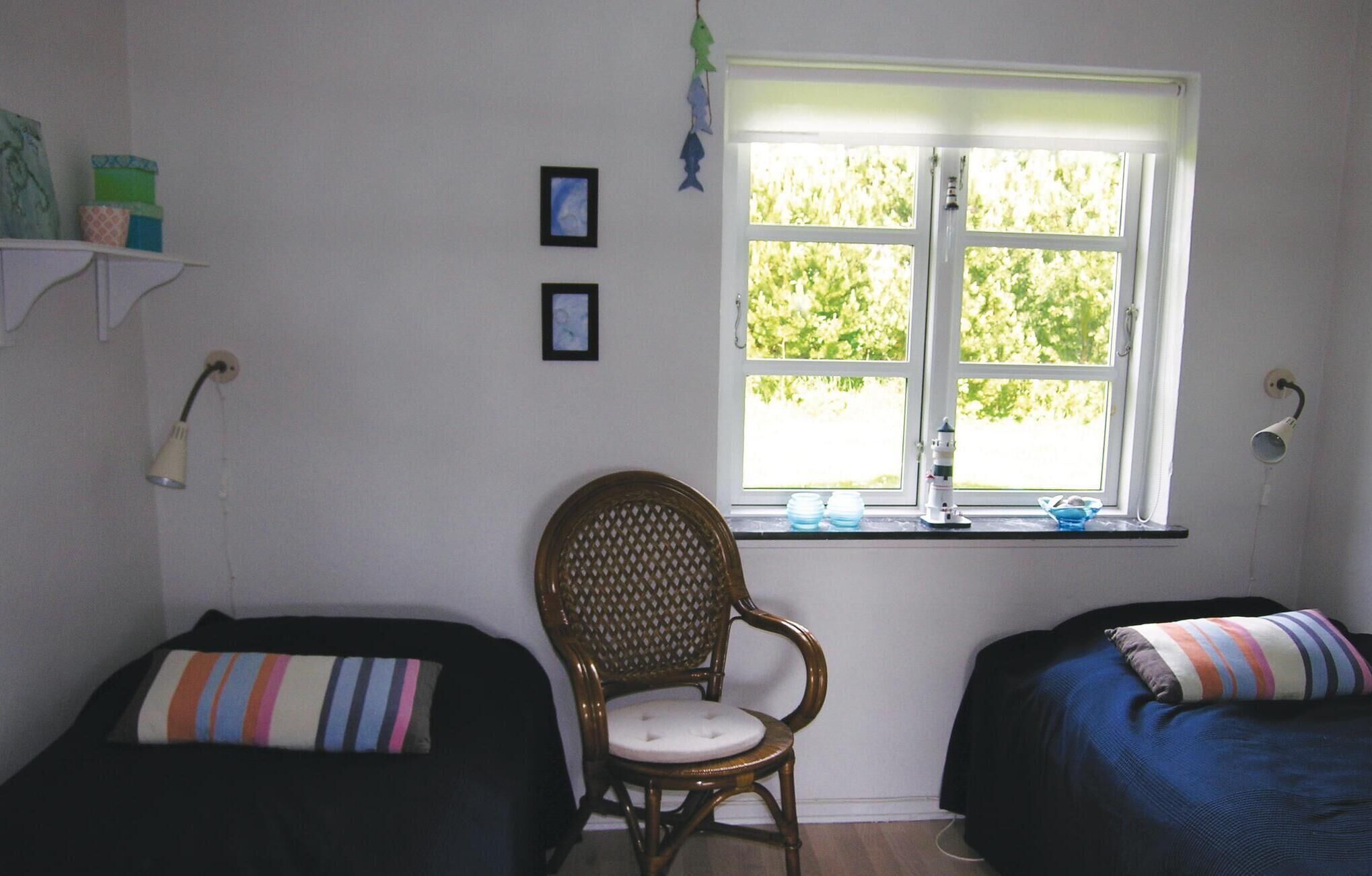 Une chambre avec deux lits, une chaise, une fenêtre donnant sur un espace verdoyant et une étagère avec divers objets.