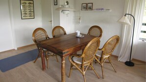 Ein Esszimmer mit Holztisch und Korbstühlen, einer weißen Pendelleuchte und einem gerahmten Bild von Fischen an der Wand.