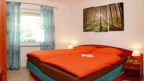 Ein Schlafzimmer mit Bett, Vorhängen, Nachttisch, Lampe und einem Bild an der Wand.