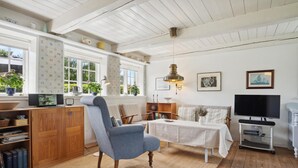 A cozy living room with a blue armchair, a wooden cabinet, a television, and a table with a white tablecloth. - 3 bedroom beautiful home in Fanø (Fanø)