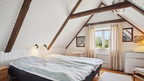 A bedroom with a sloped ceiling, a bed, a bedside table, a dresser, a window with curtains, and a framed picture on the wall. - 3 bedroom beautiful home in Fanø (Fanø)