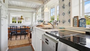 A kitchen with white cabinets, a black countertop, and a window with blue floral tiles. - 3 bedroom beautiful home in Fanø (Fanø)
