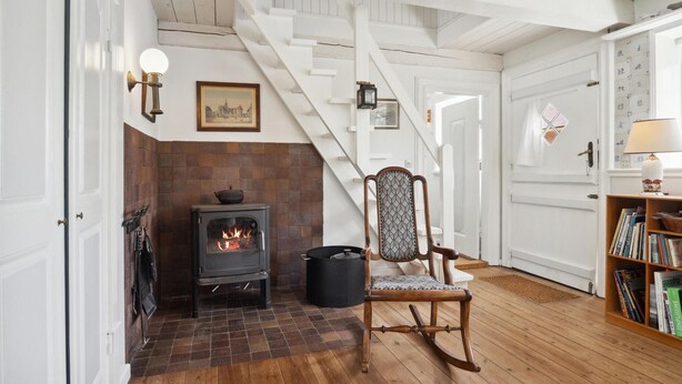 A cozy room with a fireplace, a wooden chair, a bookshelf, and a staircase. - 3 bedroom beautiful home in Fanø (Fanø)