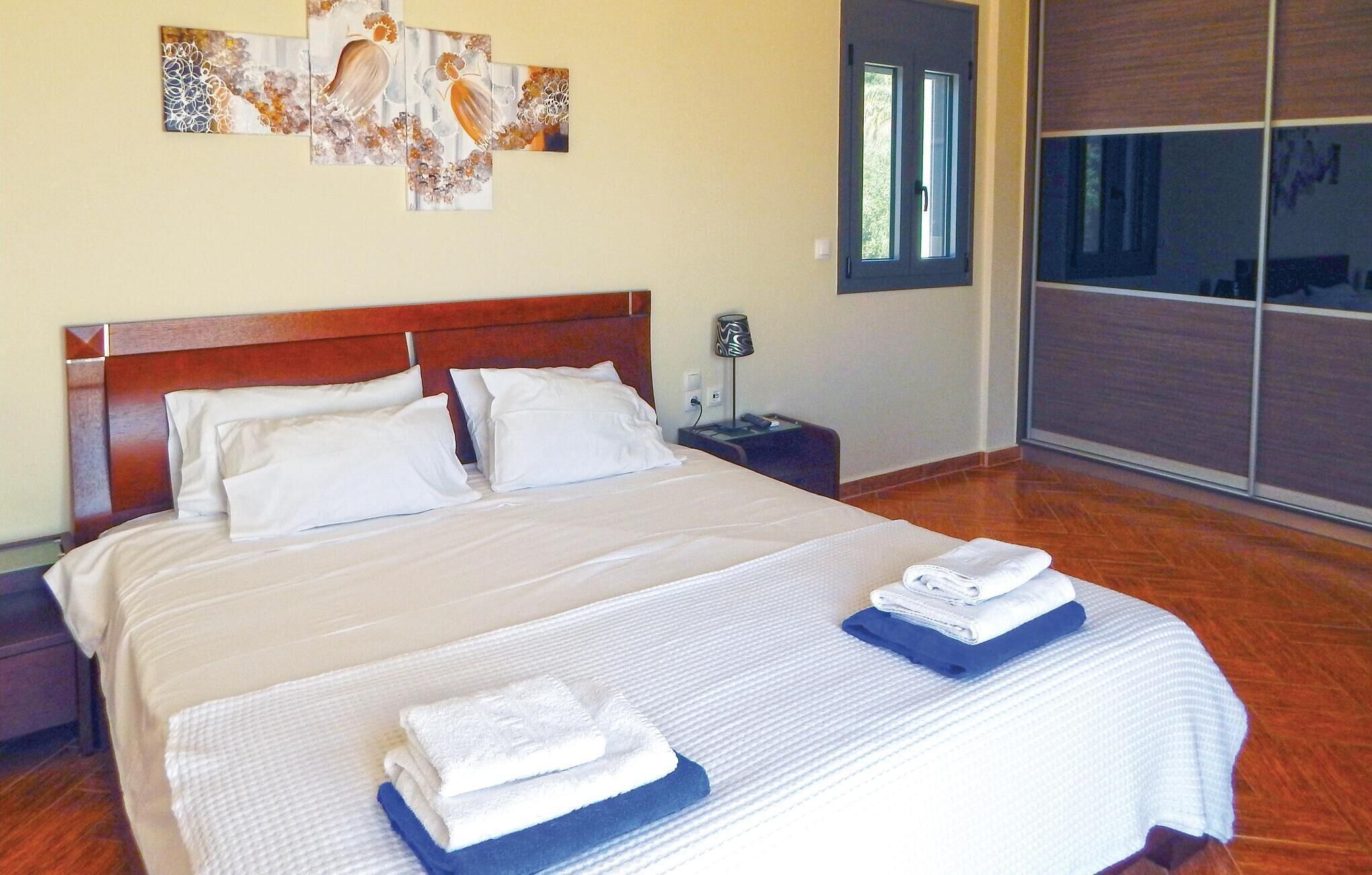 A hotel room with a large bed, two pillows, a nightstand with a lamp, and artwork on the wall.