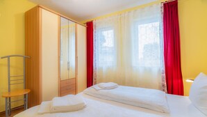 Ein Hotelzimmer mit zwei Betten, einem Kleiderschrank, einem Sessel und einem Fenster mit roten Vorhängen.