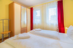 Una camera d'albergo con due letti, un armadio, una sedia e una finestra con tende rosse.