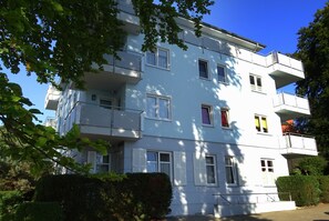 Ein mehrgeschossiges Wohngebäude mit Balkonen, weißen Fensterläden und blauem Himmel.