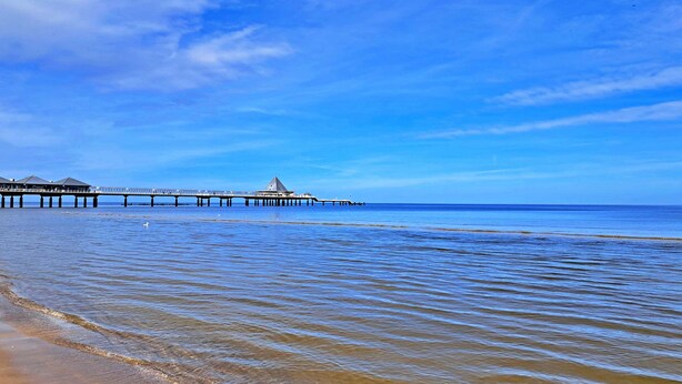 Eine Mole, die sich in ruhiges Wasser erstreckt, mit blauem Himmel.
