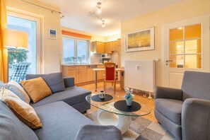 Ein modernes Wohnzimmer mit einem grauen Sofa, einem Glastisch und einem Essbereich mit einem roten Stuhl.
