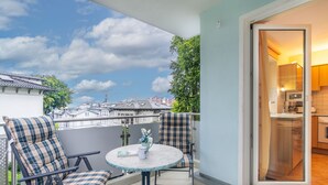 Ein Balkon mit zwei Stühlen und einem Tisch, Blick auf Gebäude und eine Tür zu einer Küche.