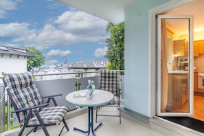 A balcony with two chairs and a table, a view of buildings, and a door leading to a kitchen.