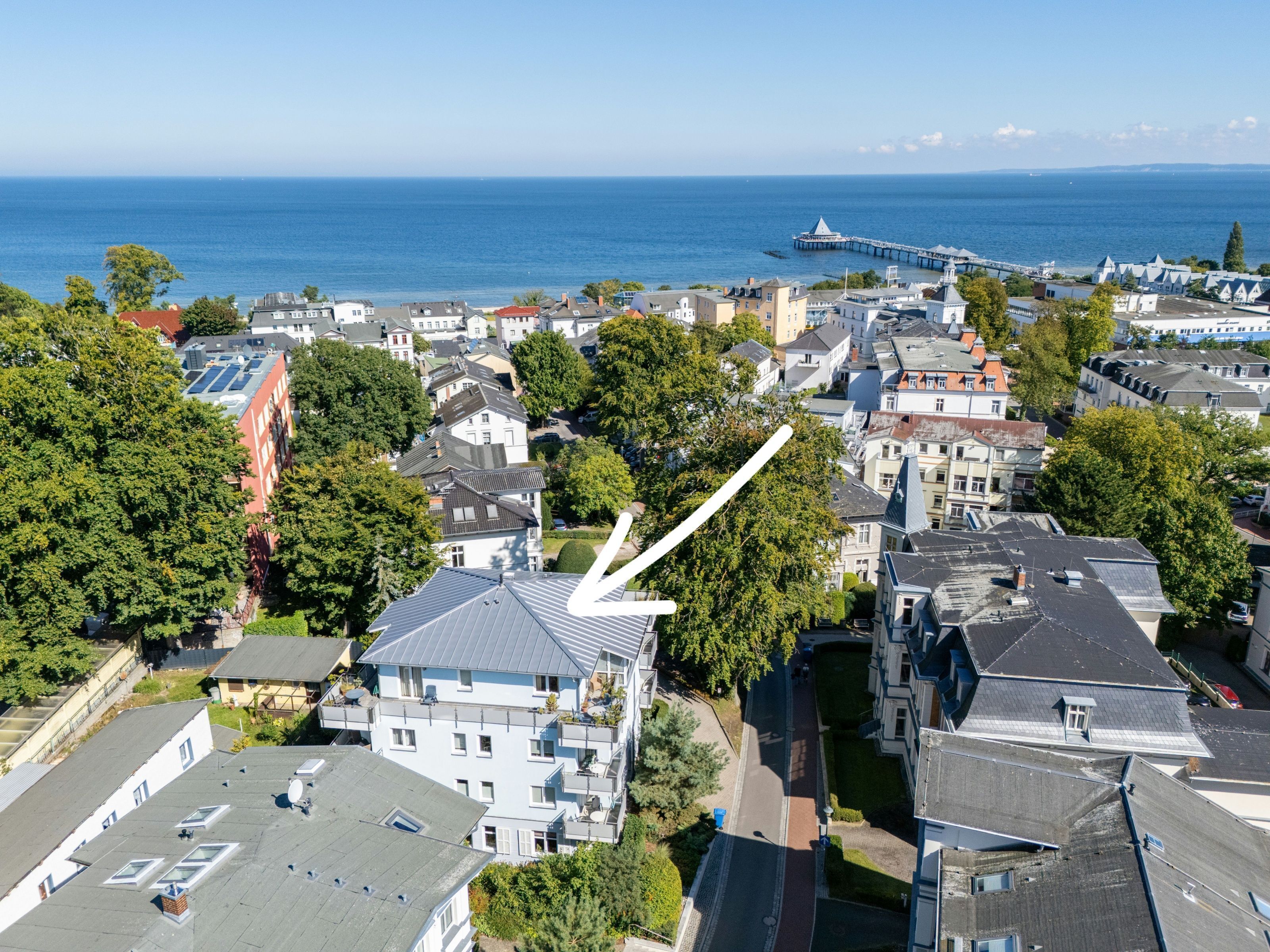 Une vue aérienne d’une ville côtière, avec un mélange de bâtiments résidentiels, un imposant bâtiment blanc doté d’un toit en forme de flèche, et une jetée qui s’avance dans la mer.