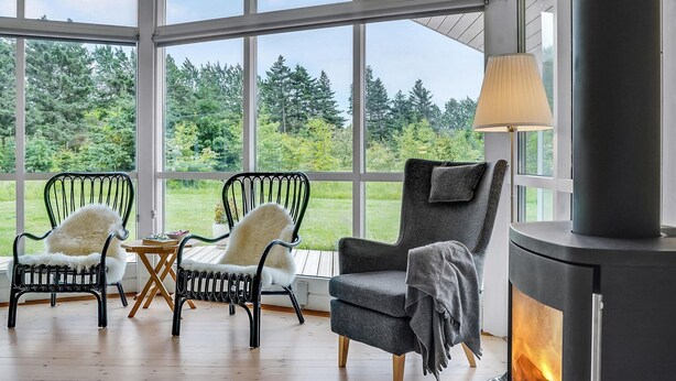 Une pièce chaleureuse avec une grande fenêtre, deux fauteuils recouverts de peaux de bêtes, une cheminée et une lampe.