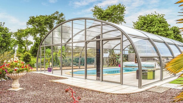 Una estructura tipo invernadero con techo de cristal, rodeada por un jardín con diversas plantas y flores.