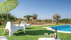 A poolside area with white lounge chairs, a green umbrella, and a table with wine glasses and a bottle.